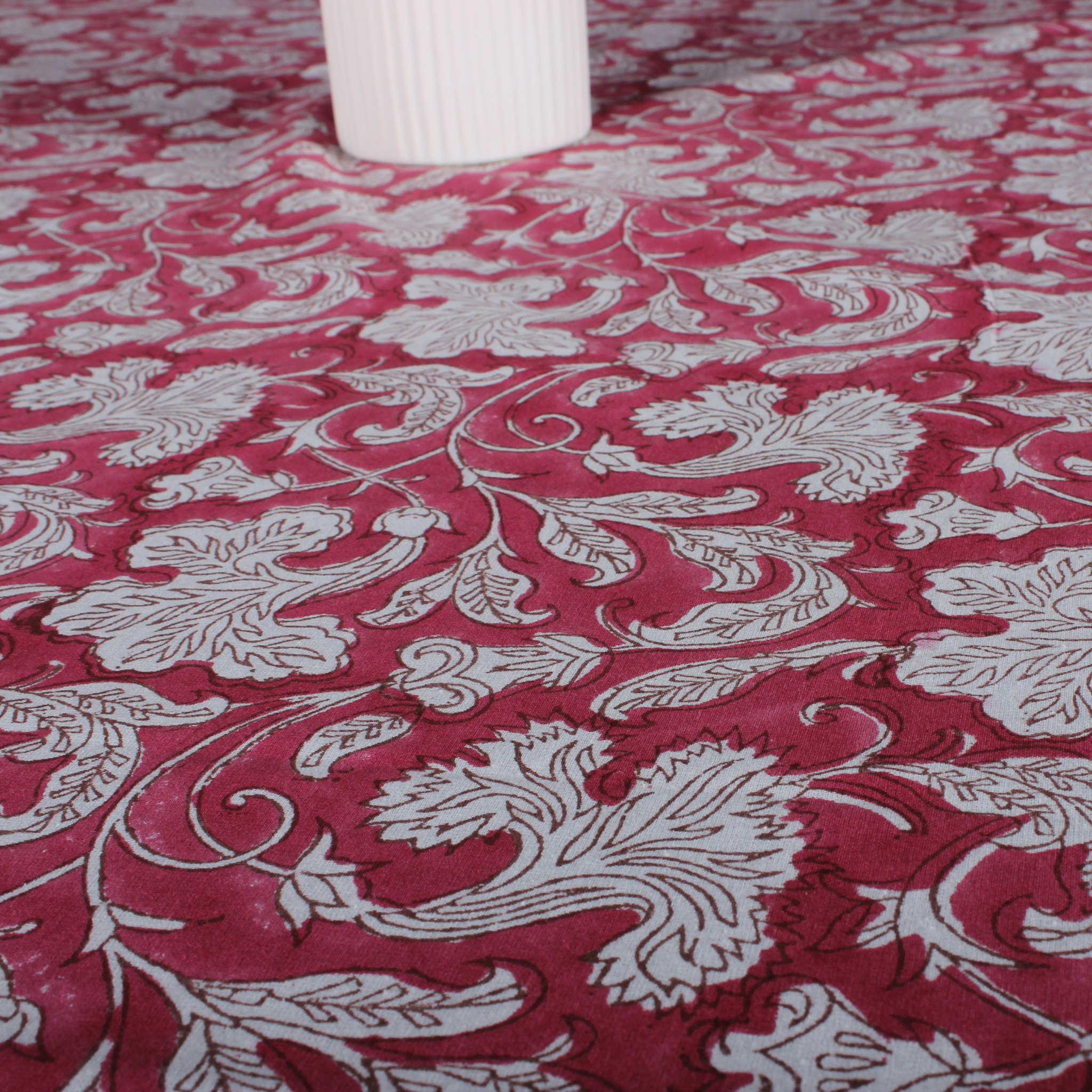 Red fabric with white floral patterns, partially covering a white cylindrical object.