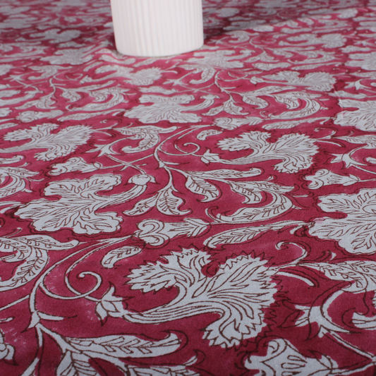 Red fabric with white floral patterns, partially covering a white cylindrical object.