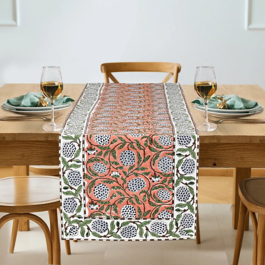 Decorative table runner with floral pattern on a wooden table with glasses and plates.