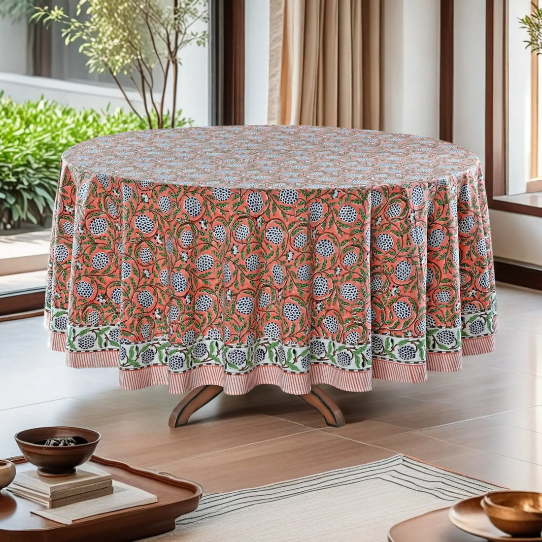 Round table with a patterned tablecloth in a room with plants and a window.