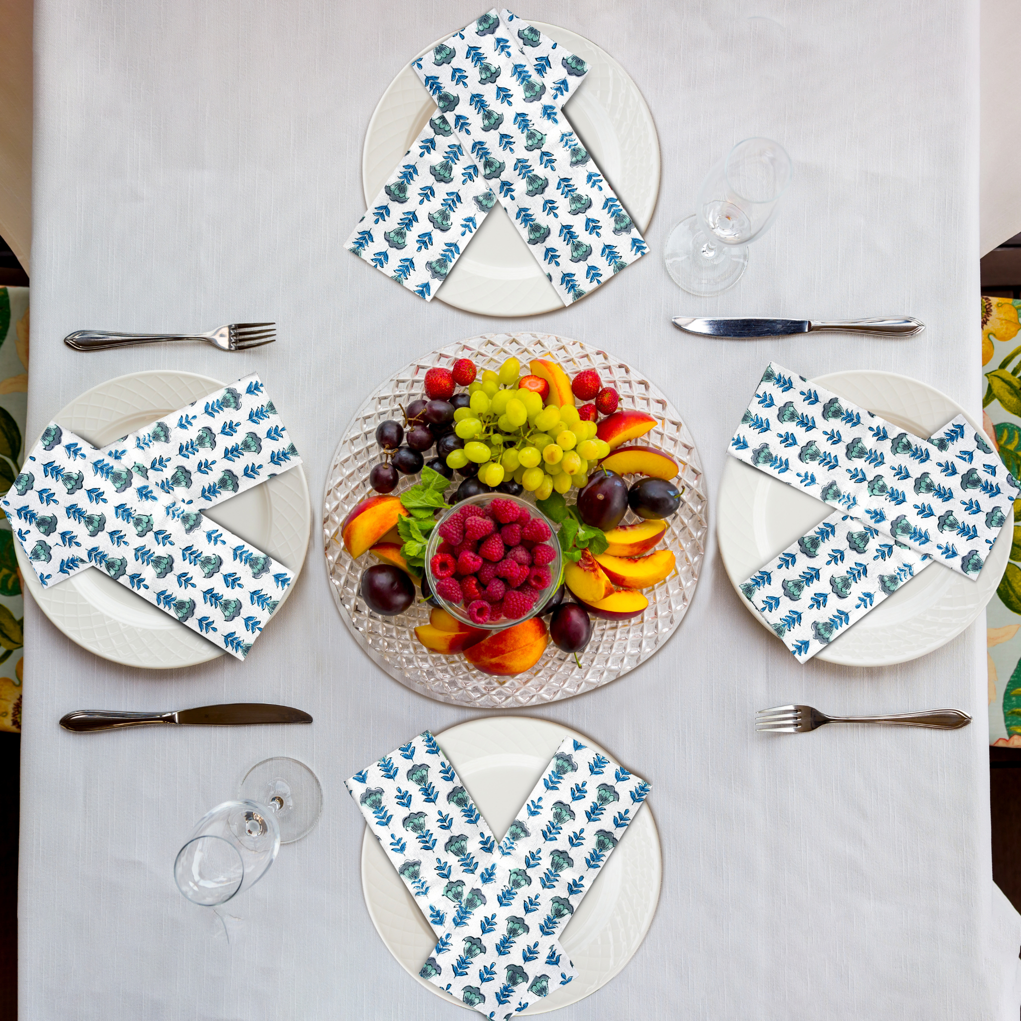 Table setting with plates, napkins, and a fruit platter on a white tablecloth.