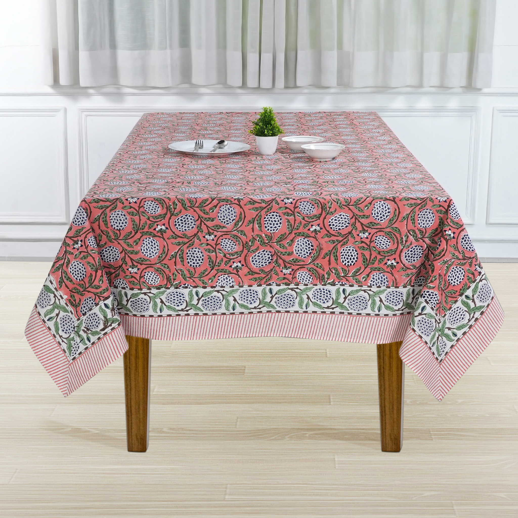 Tablecloth with floral pattern on a wooden table in a room with white walls and curtains.
