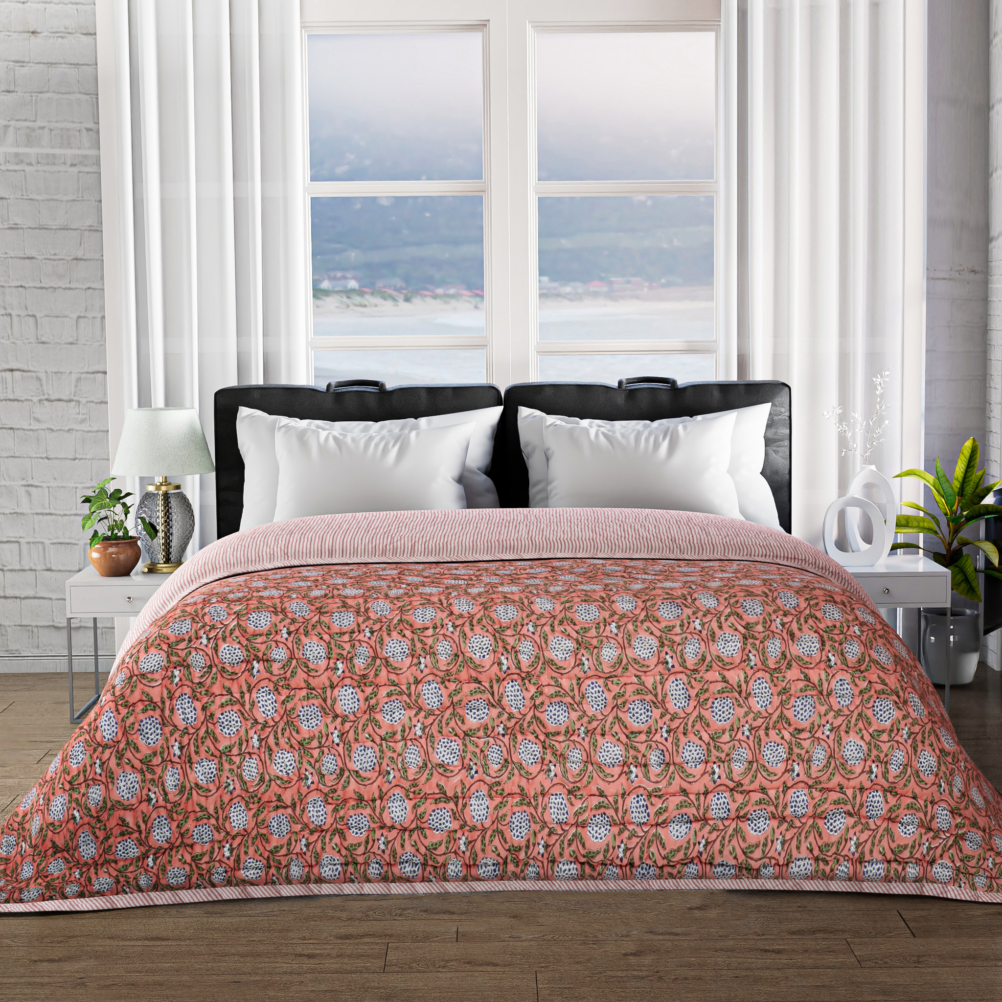 Bed with pink floral comforter in a room with large windows and plants.