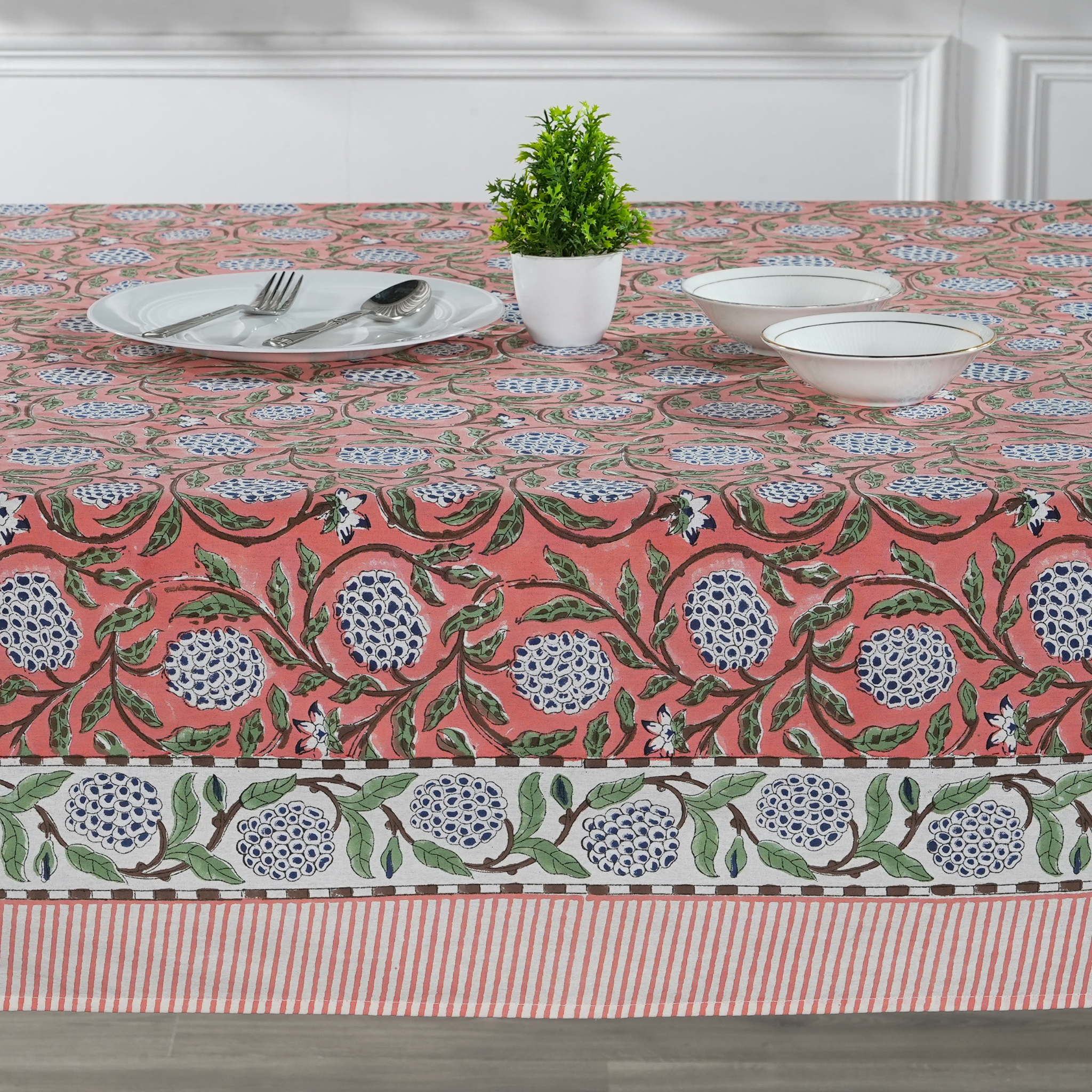 Tablecloth with floral pattern on a dining table with plates and a plant.
