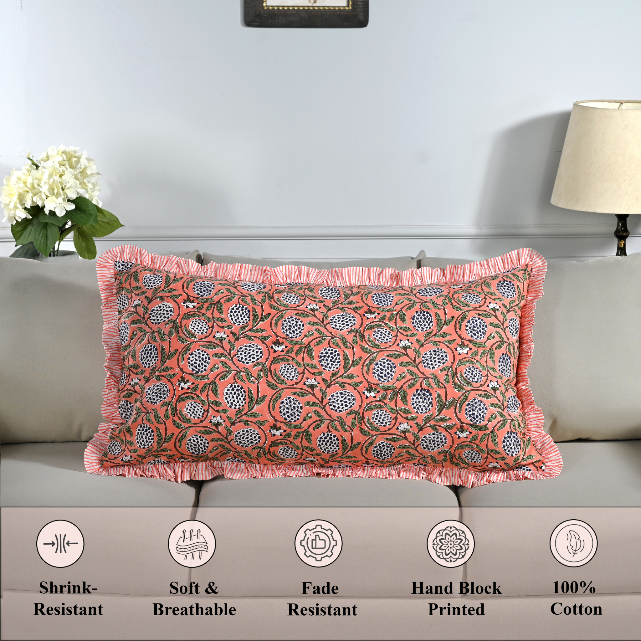 Cotton block print pillow cover placed on a bed with lamp and flowers in background.
