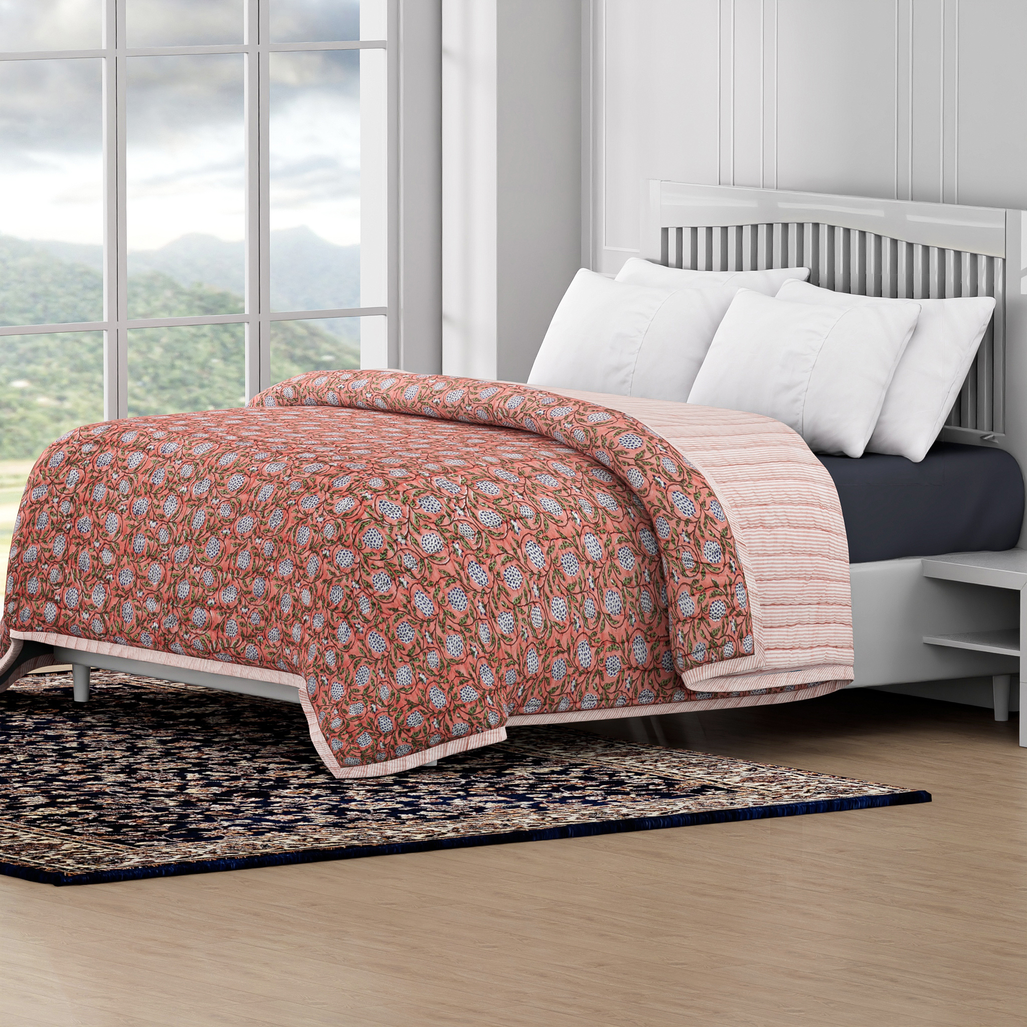 Bed with floral quilt and white pillows in a room with large windows and a view of mountains.