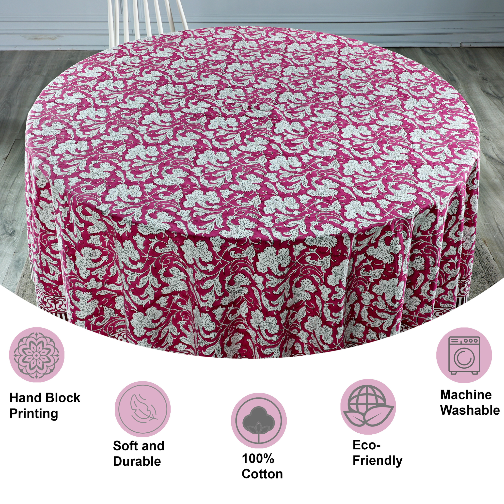 Round table covered with a pink floral tablecloth on a wooden floor.