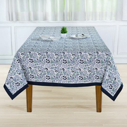 Tablecloth with floral pattern on a wooden table in a room with white walls and curtains.