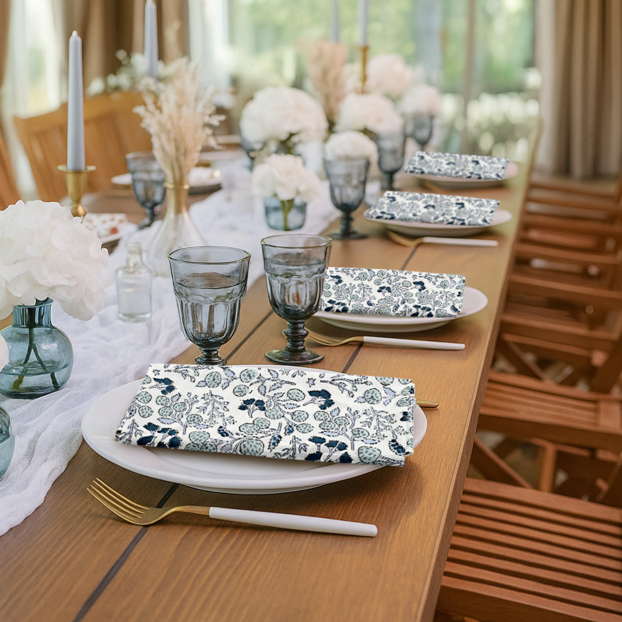 Elegant table setting with floral plates, glasses, and napkins in a bright room.