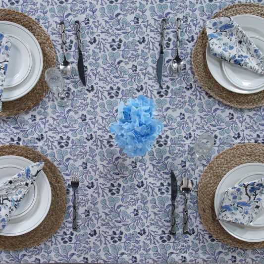 Table setting with floral tablecloth, plates, cutlery, and napkins on a patterned surface.