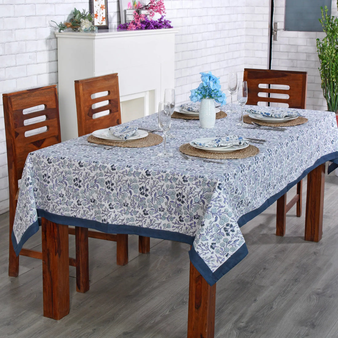 Dining table set with a floral tablecloth in a room with white brick walls.