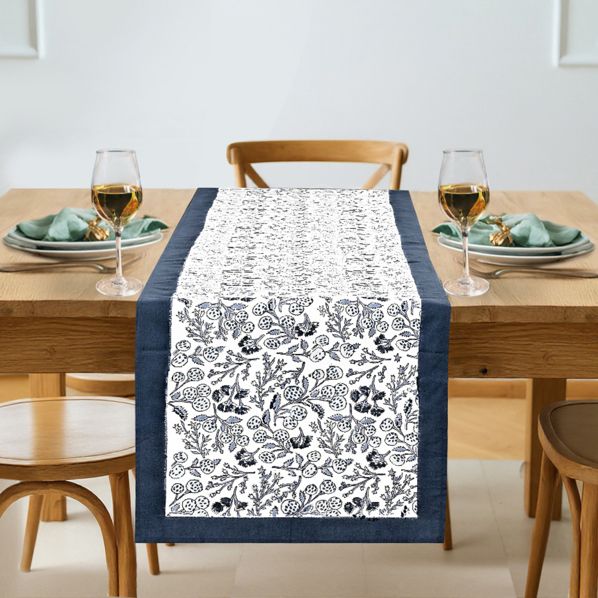 Dining table set with a floral patterned table runner, glasses, and plates.