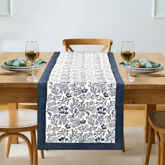 Dining table set with a floral patterned table runner, glasses, and plates.