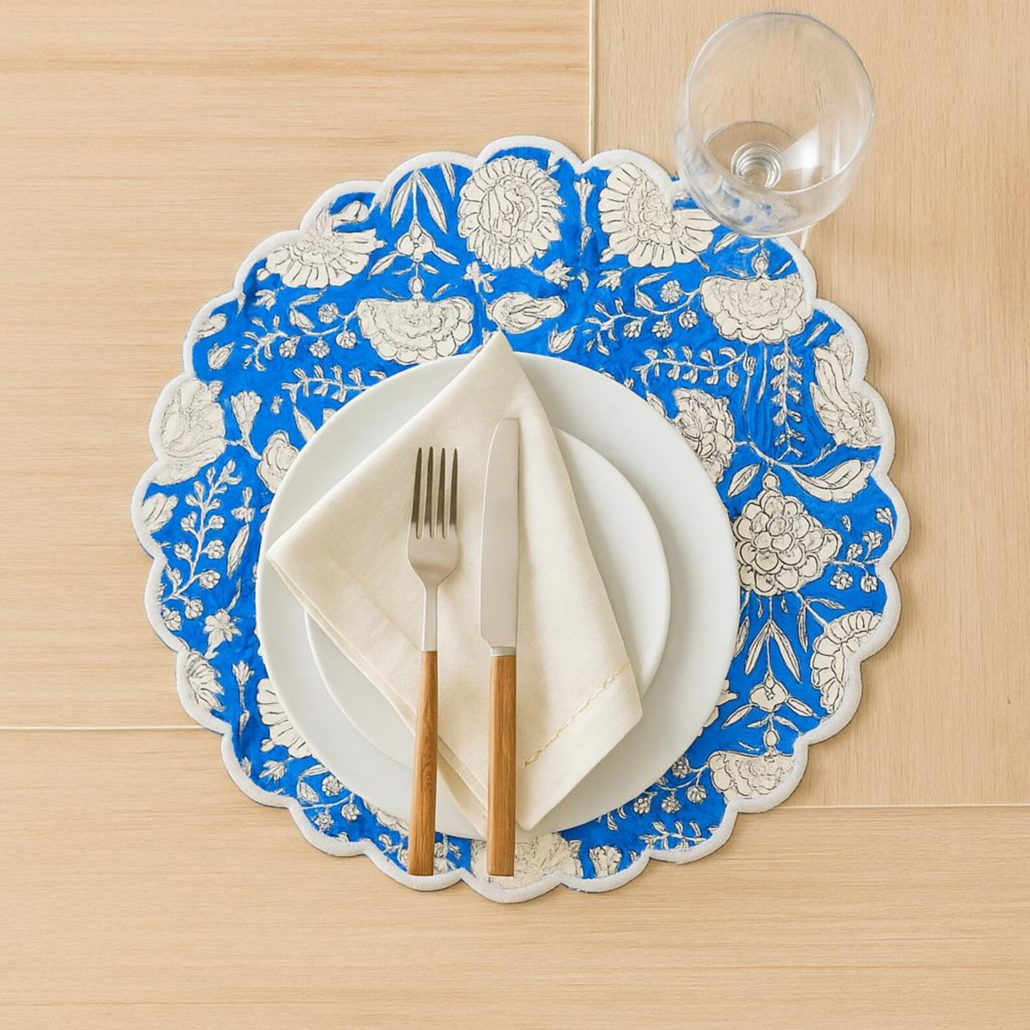 Decorative blue and white floral placemat with cutlery on a wooden surface