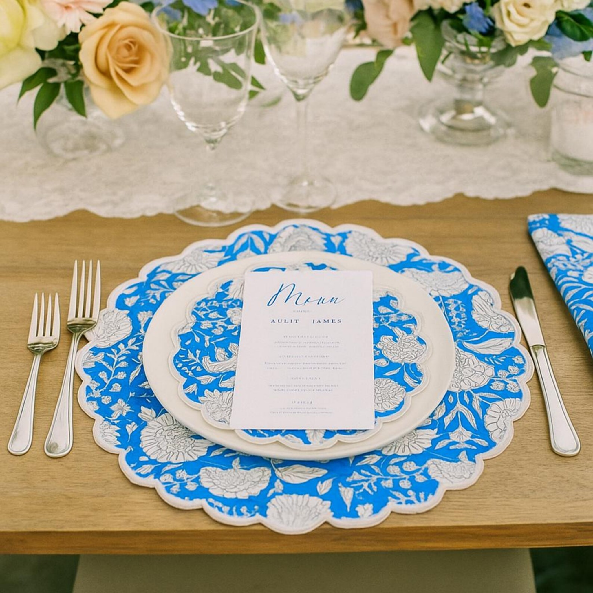 Table setting with blue and white doily, menu card, and cutlery on a wooden table.