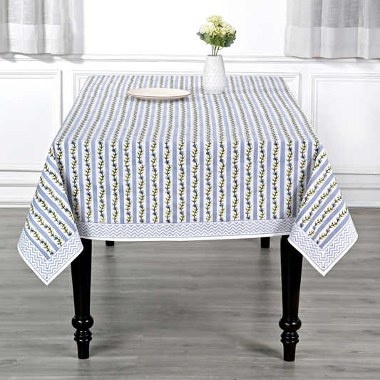 Tablecloth with floral pattern on a wooden table in a room with white curtains.