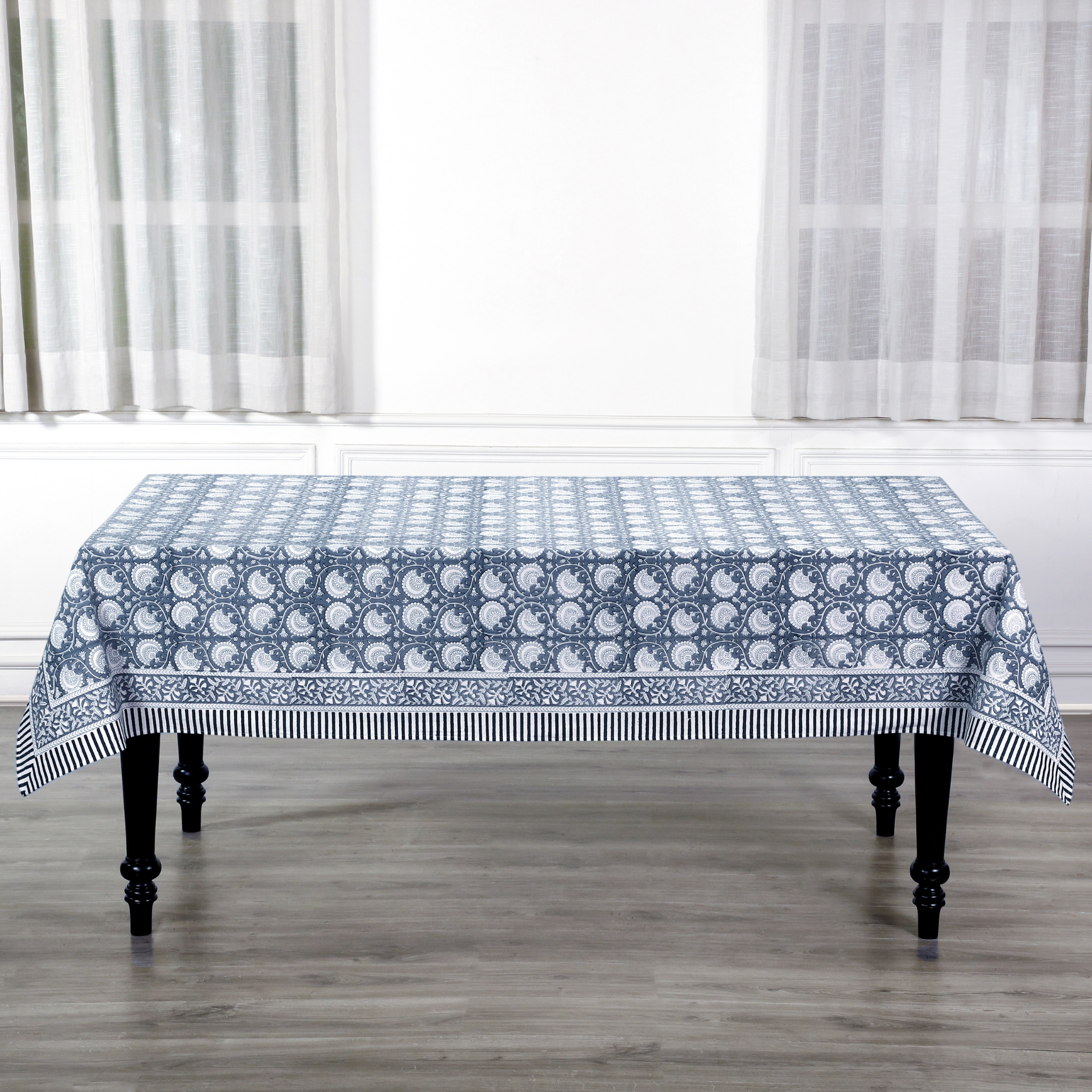 Tablecloth with blue and white pattern on a wooden table in a room with white curtains.