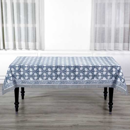Tablecloth with blue and white pattern on a wooden table in a room with white curtains.