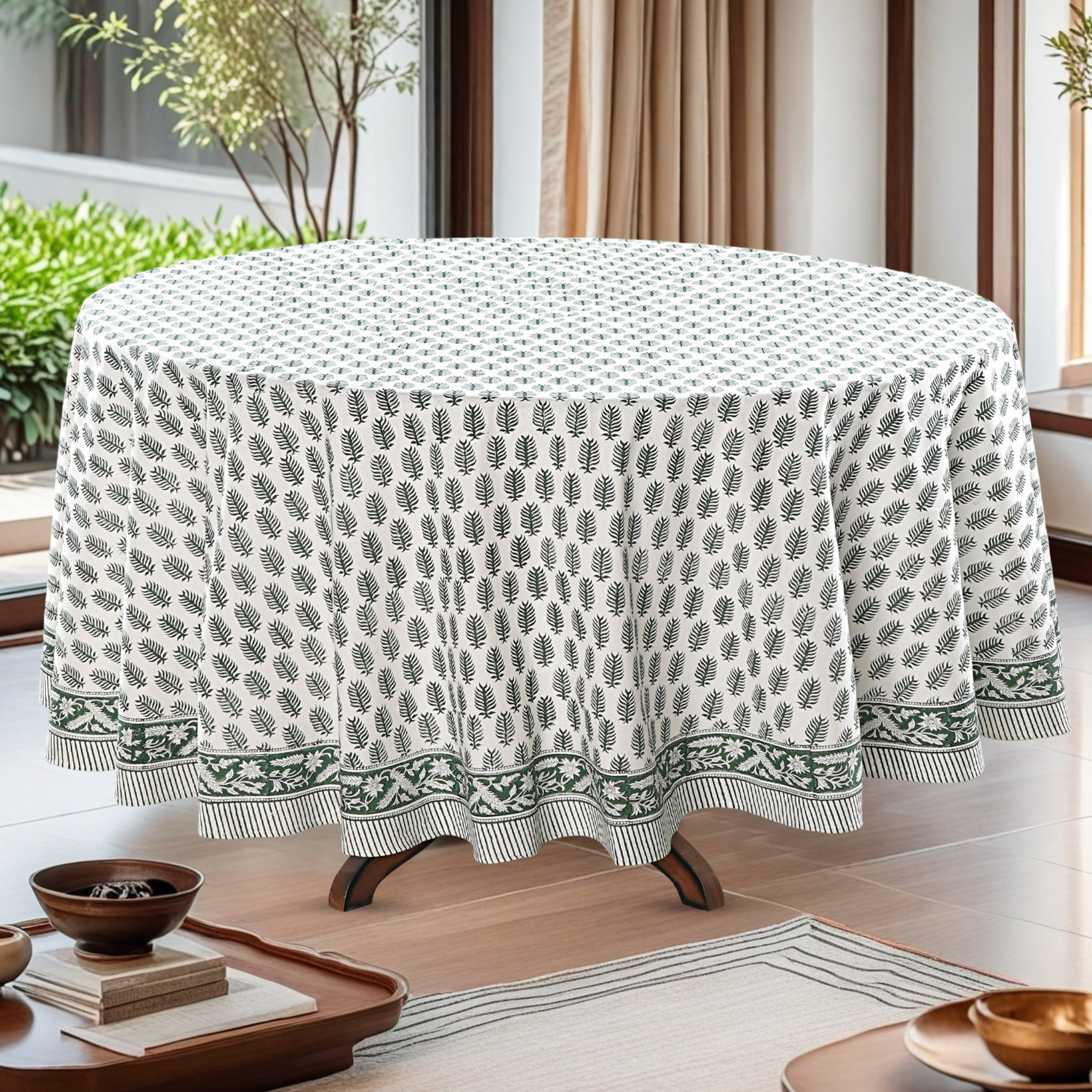 Round table with a green and white patterned tablecloth in a room with plants and curtains.