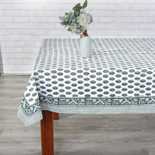 Tablecloth with leaf pattern on a wooden table against a white brick wall.