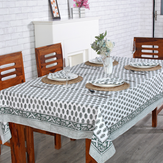 Dining table set with a patterned tablecloth, plates, and chairs in a room.