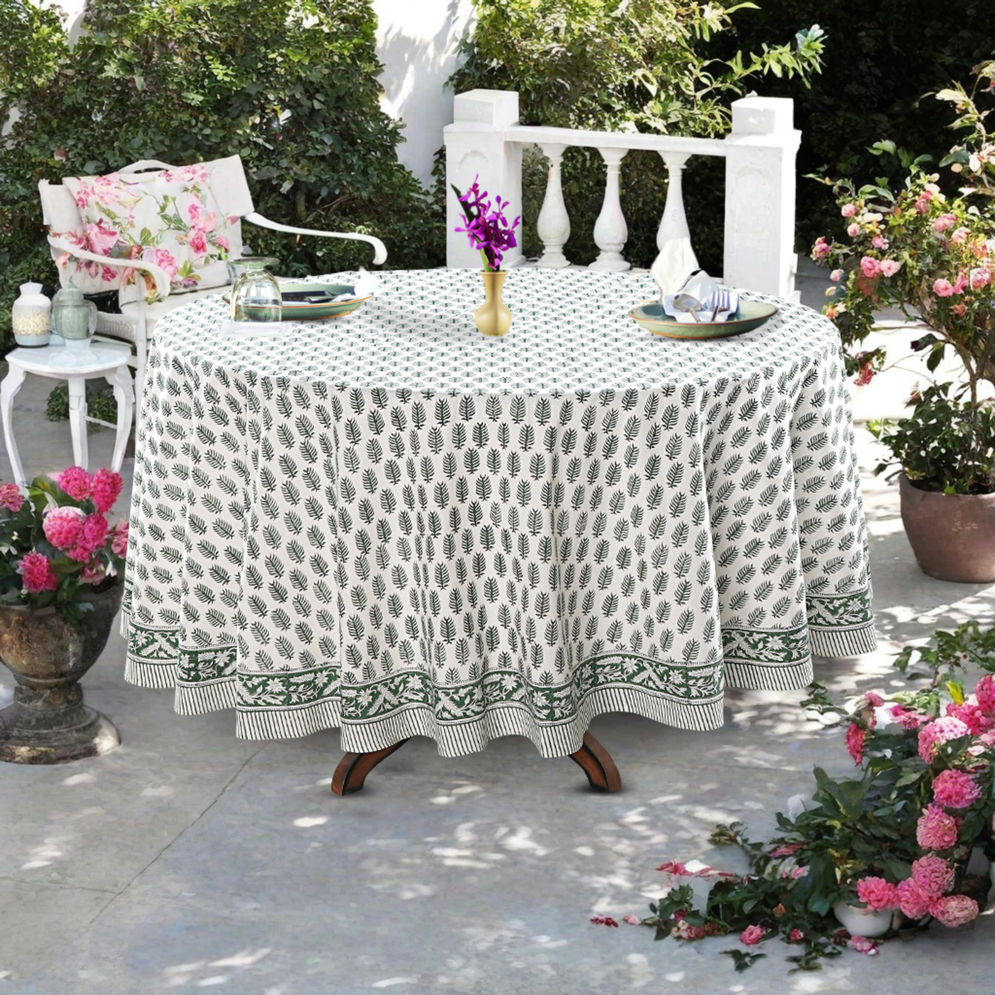 Outdoor table setting with a patterned tablecloth, chairs, and floral arrangements.