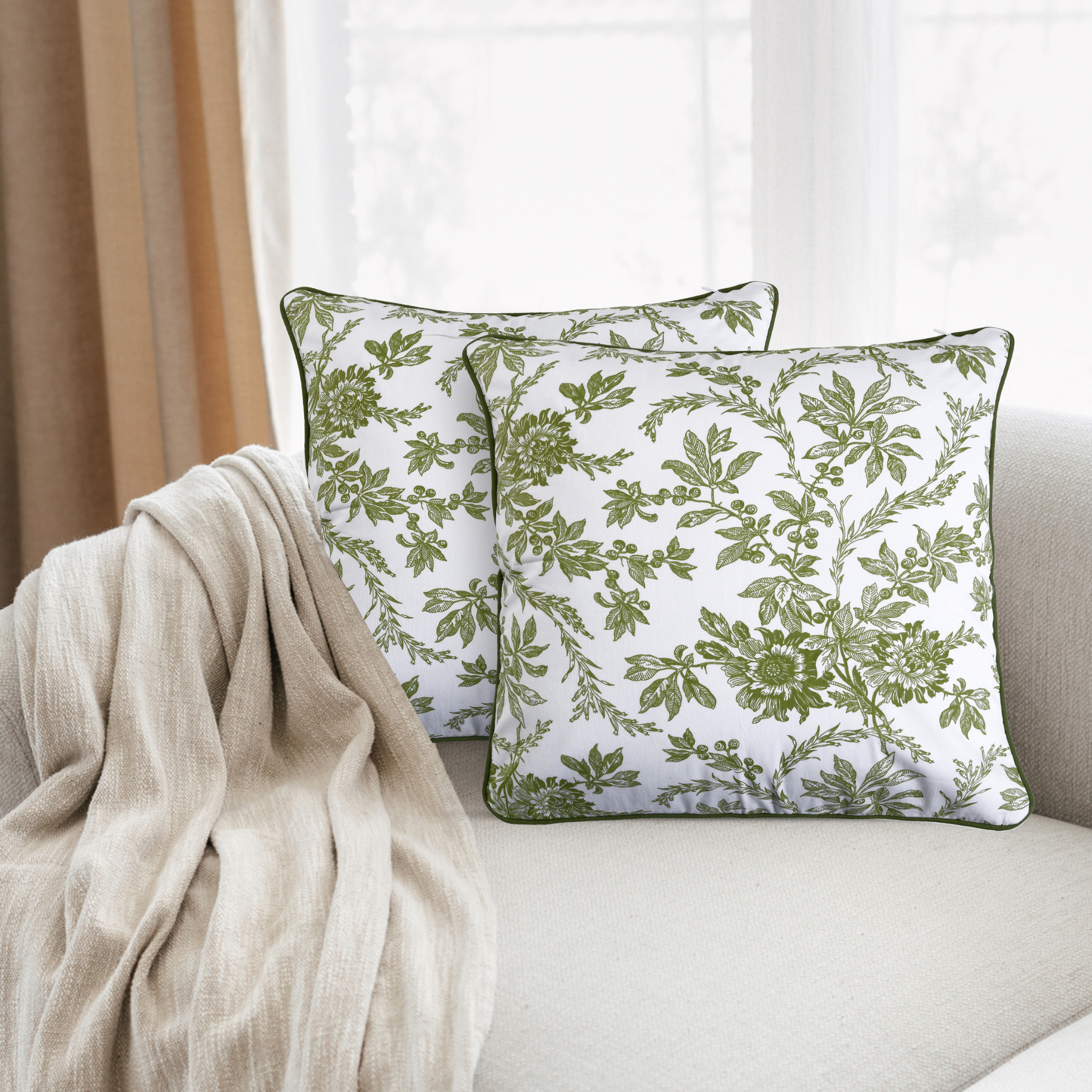 Green leaf-patterned pillows on a beige sofa with a neutral curtain in the background