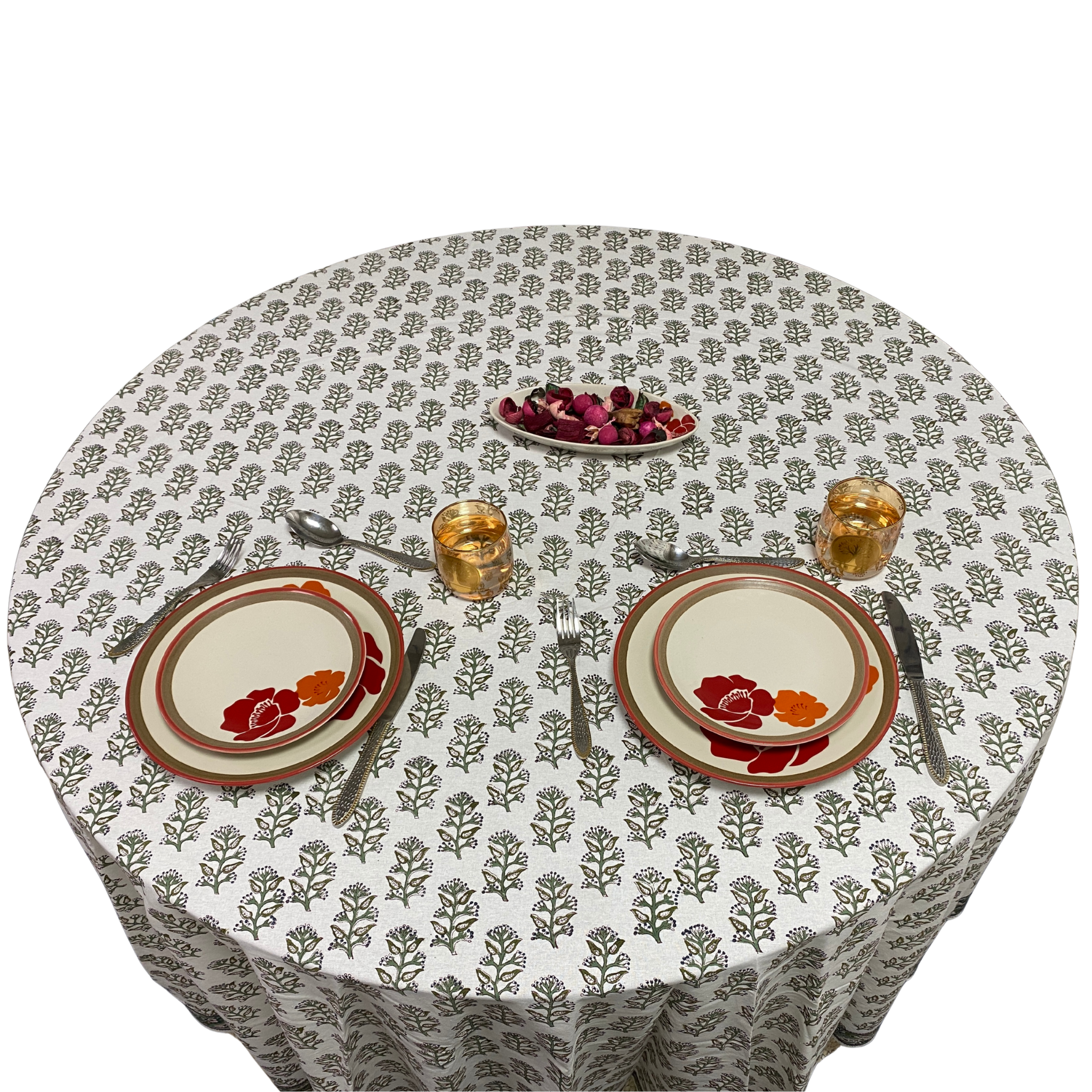 Round table with floral patterned tablecloth, plates, cutlery, and glasses on a white background