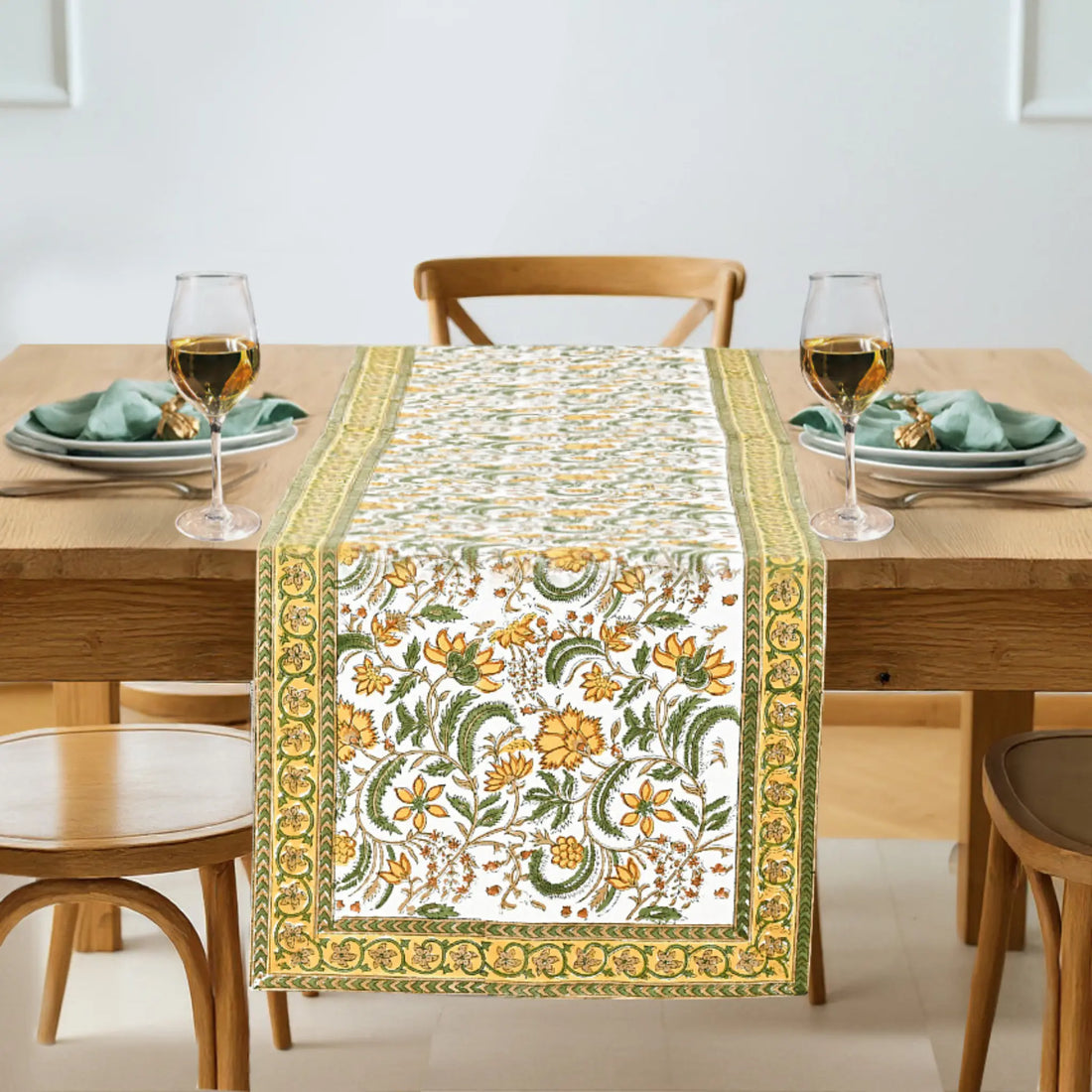Floral patterned table runner on a wooden table with glasses and plates.
