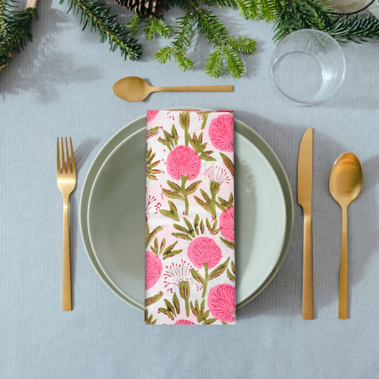 Table setting with floral-patterned napkin, gold cutlery, and greenery on a light blue tablecloth.