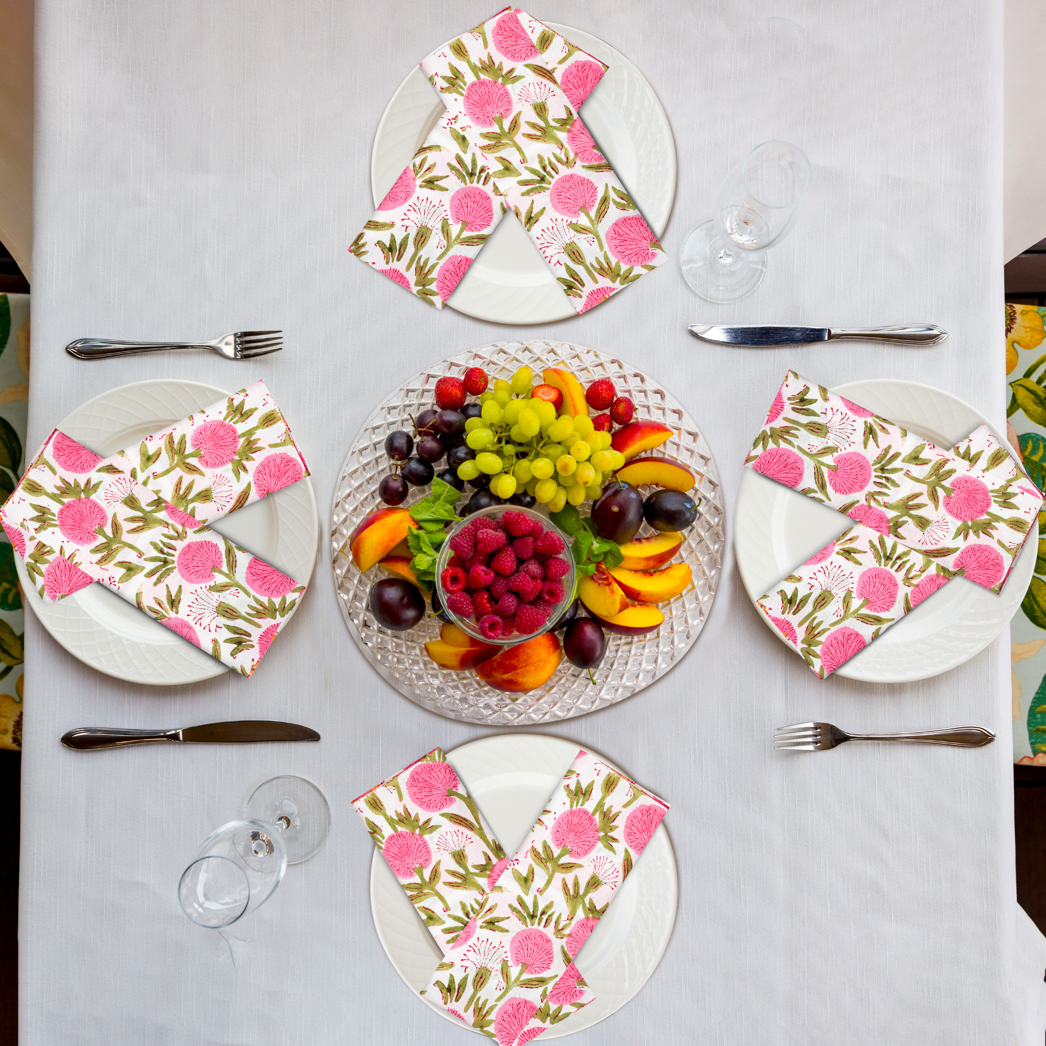 Table setting with floral napkins, plates, and a fruit platter on a white tablecloth.