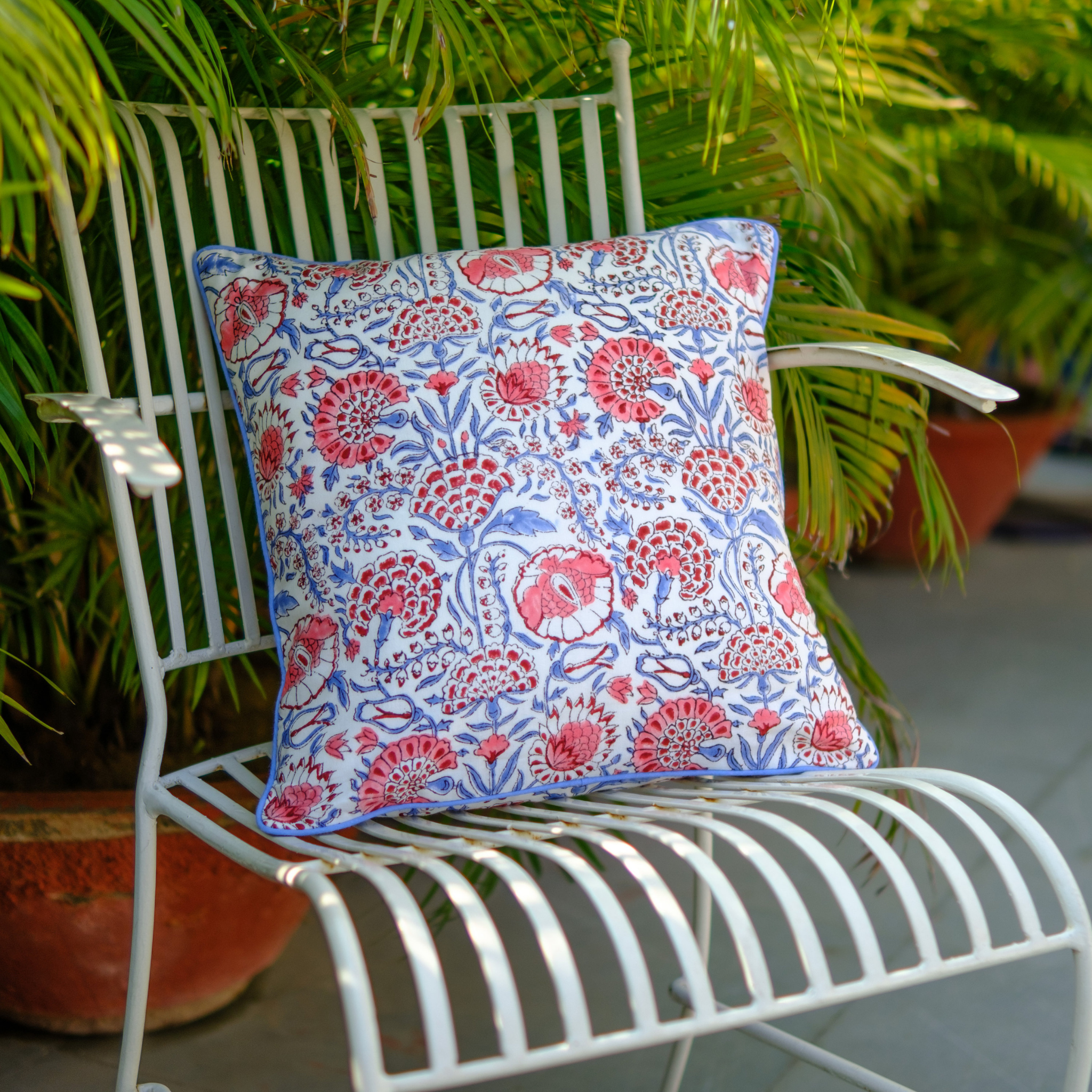Decorative pillow with floral pattern on a white metal chair outdoors.