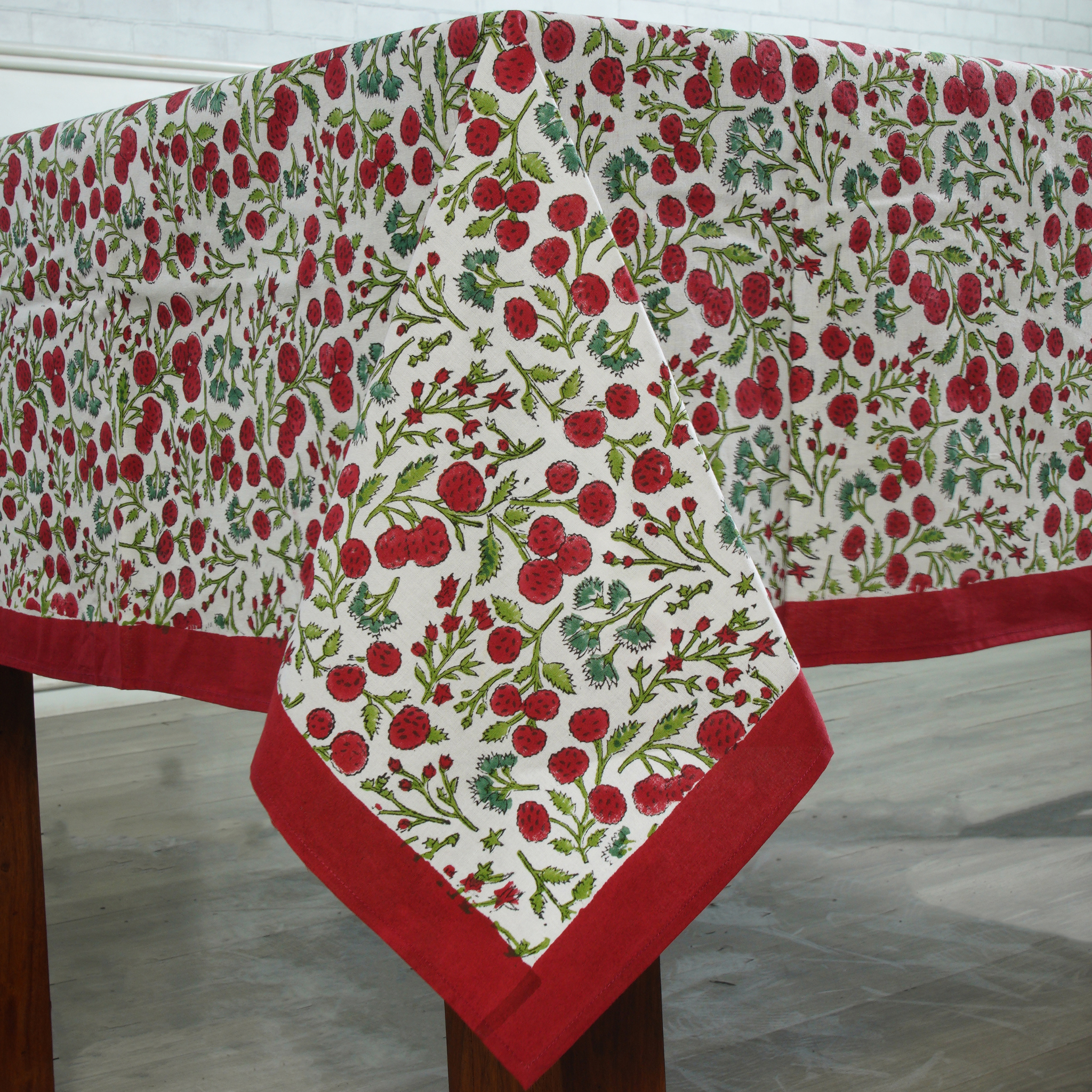 Tablecloth with red and green floral pattern on a wooden table.