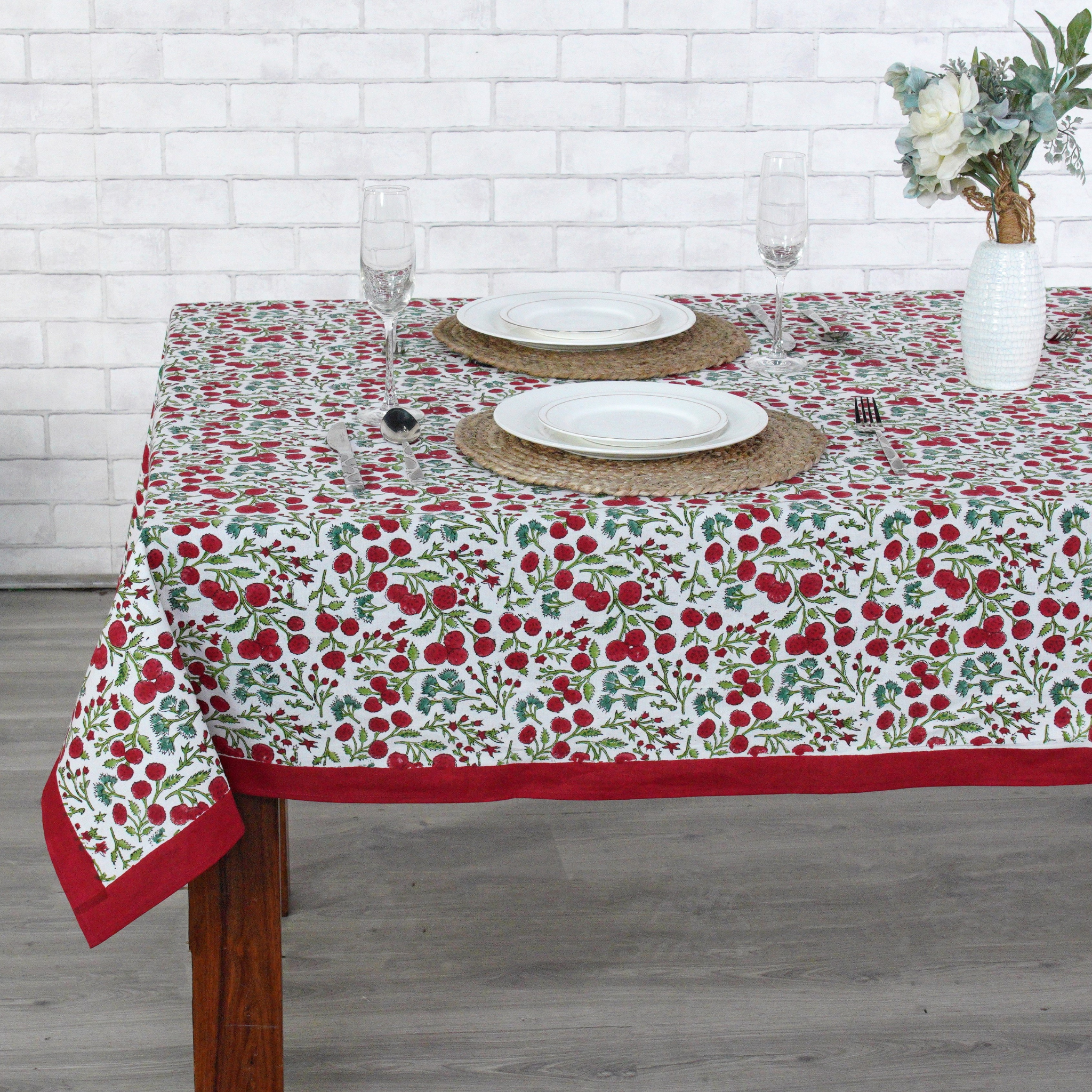 Dining table with a floral tablecloth featuring red and green patterns, set with plates and glasses.