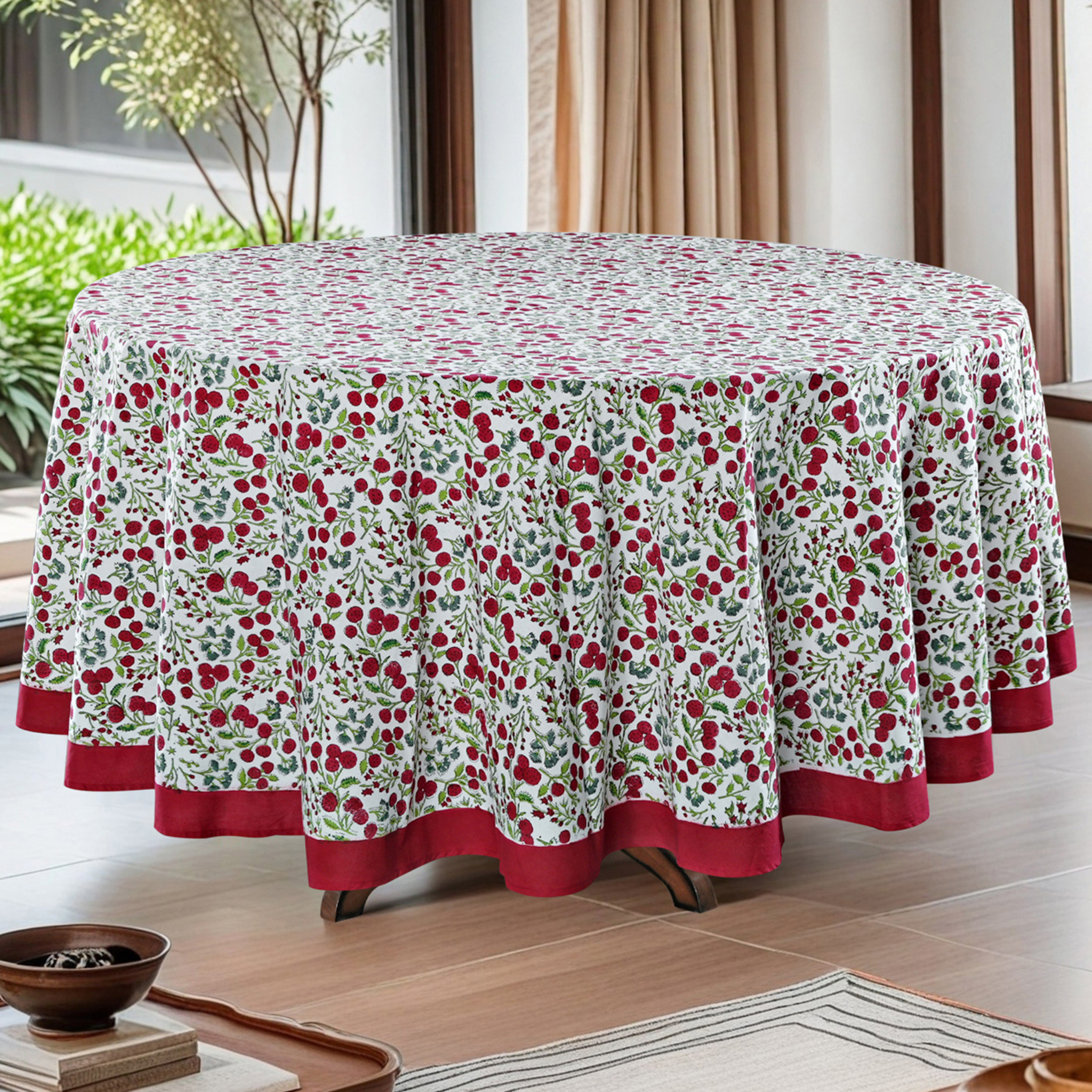 Round tablecloth with cherry pattern in a room with plants and curtains.