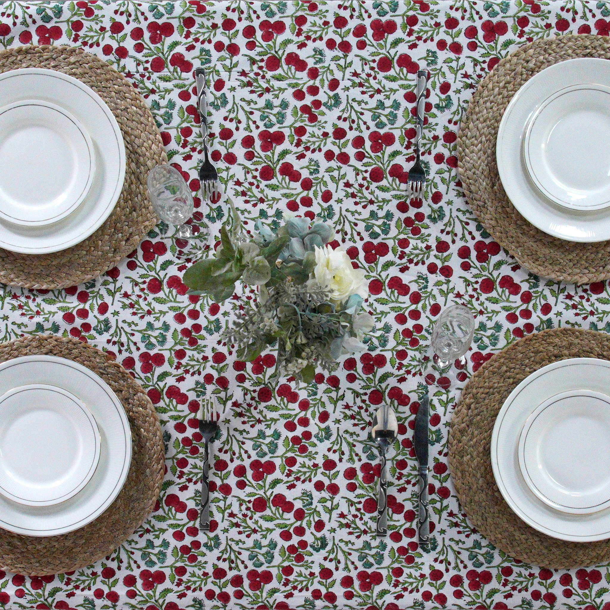 Table setting with a floral tablecloth, white plates, and woven placemats.