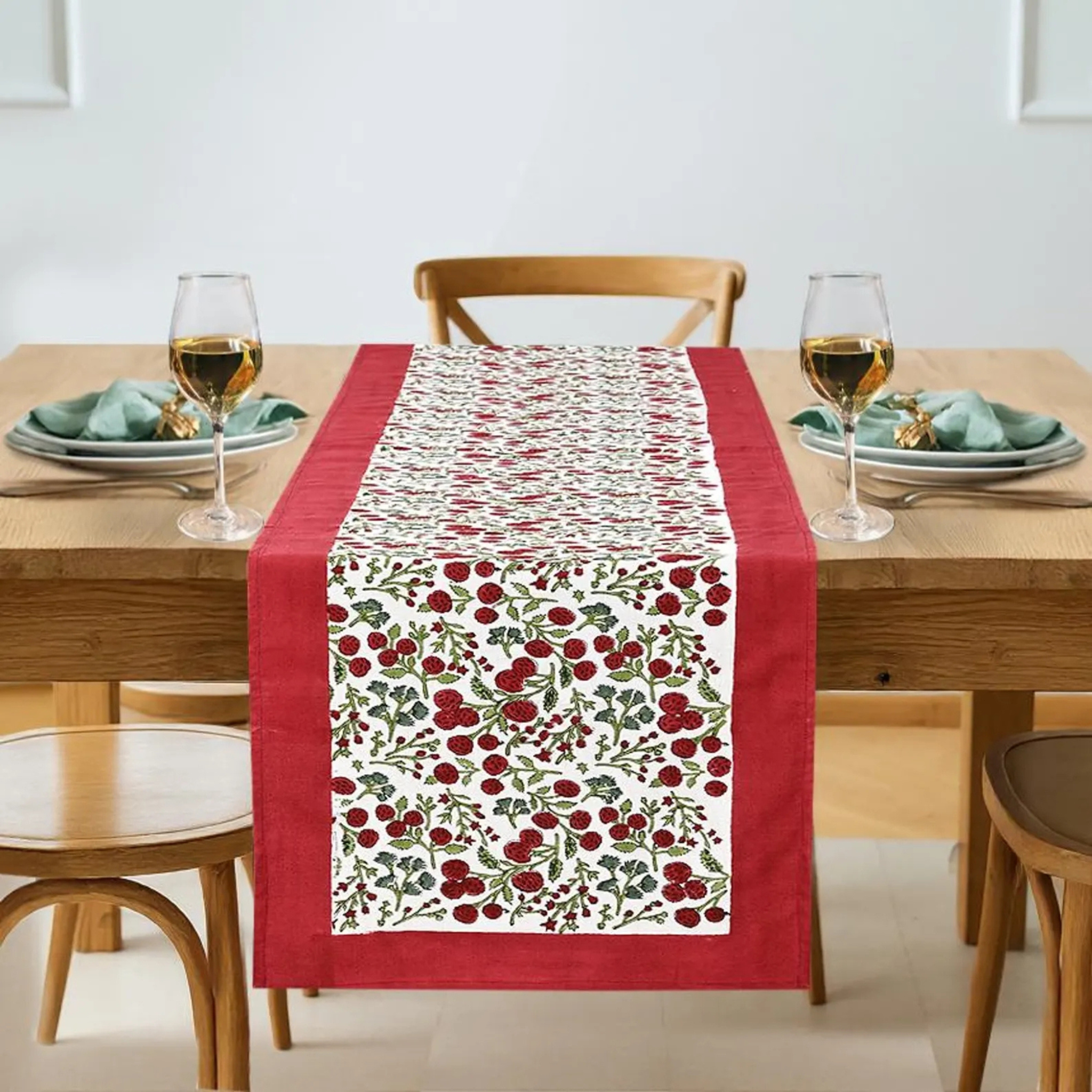 Dining table set with a red and white patterned table runner, glasses, and plates.