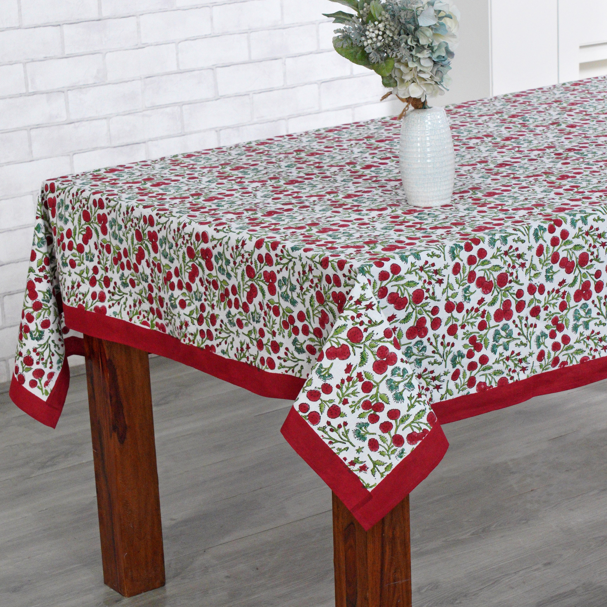 Tablecloth with floral pattern on a wooden table against a white brick wall.