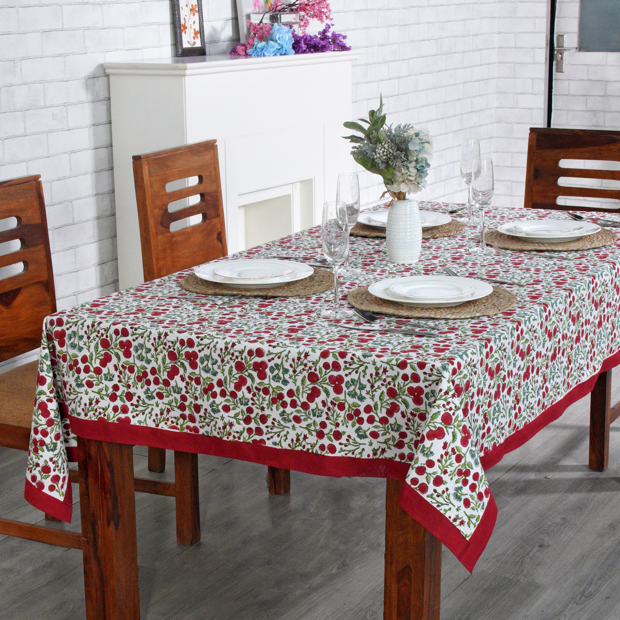 Dining table set with a floral tablecloth in a room with white brick walls.