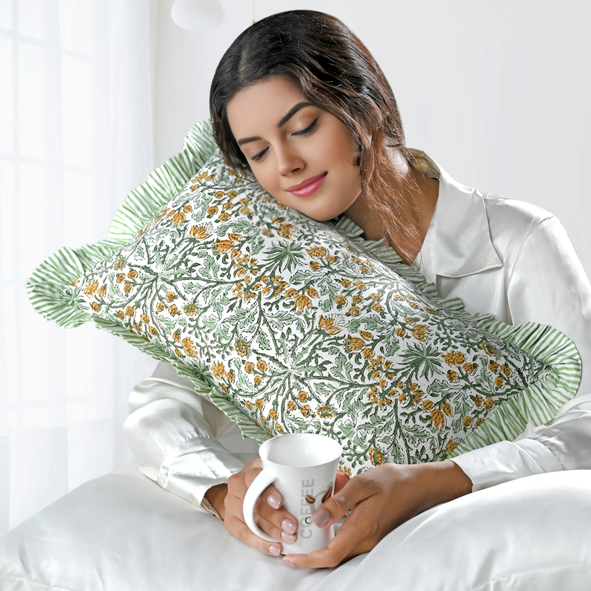 Woman holding a mug with a floral-patterned pillow behind her head on a white background