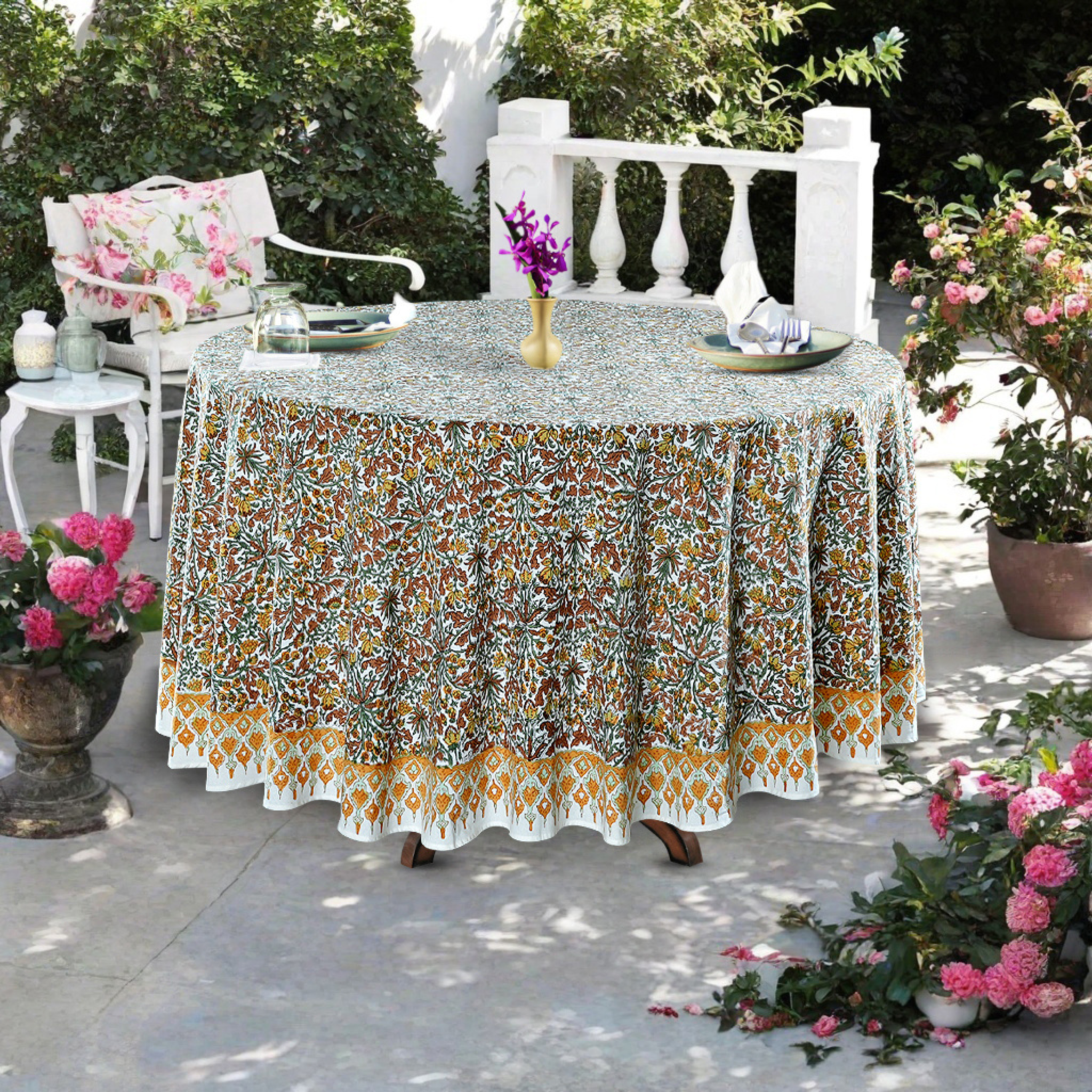 Outdoor setting with a patterned tablecloth on a table, surrounded by flowers and chairs.