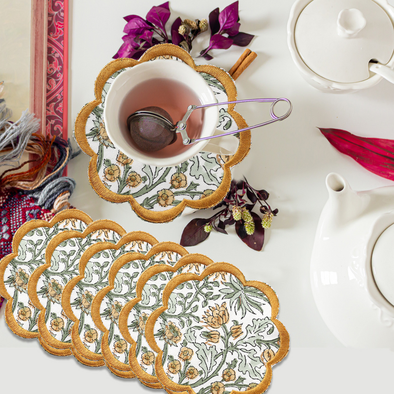 Set of floral coasters with a cup of tea and teapot on a white surface.