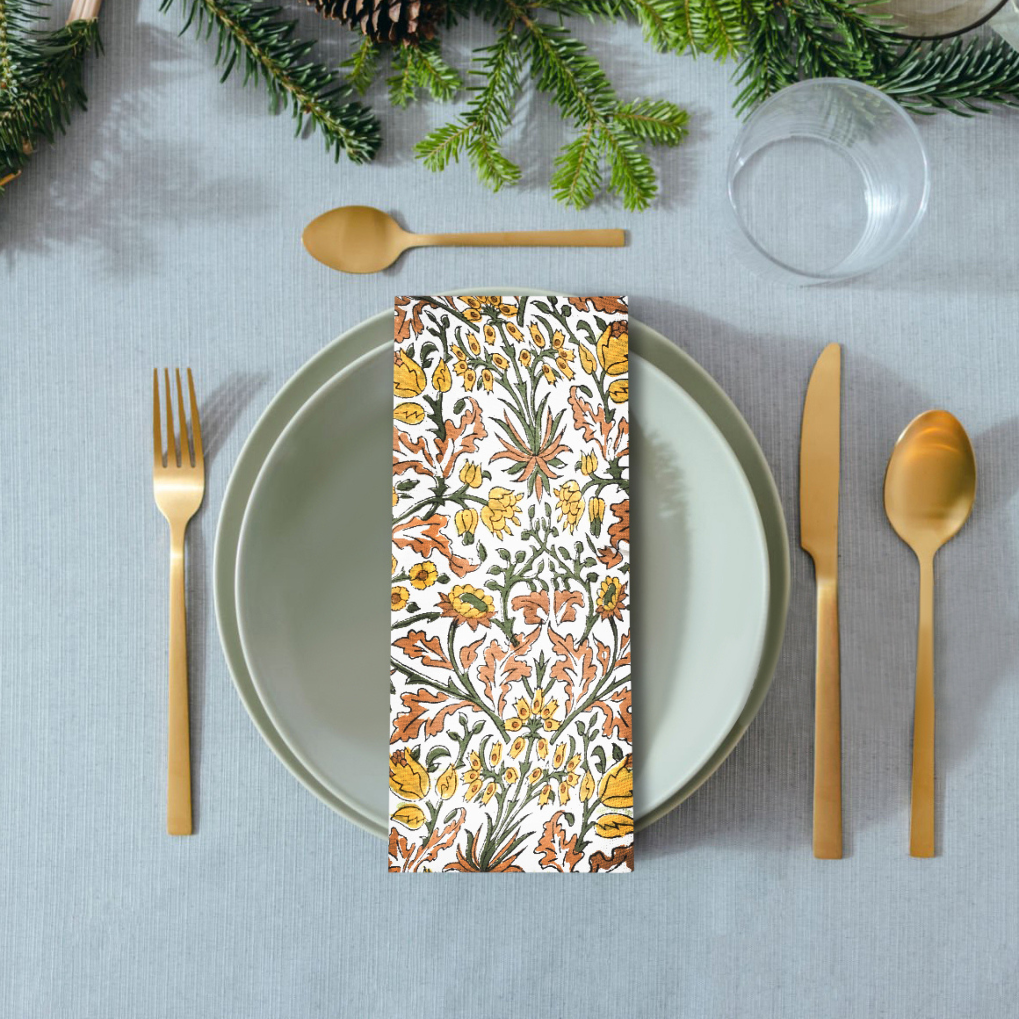 Decorative floral-patterned napkin on a table setting with gold cutlery and greenery.
