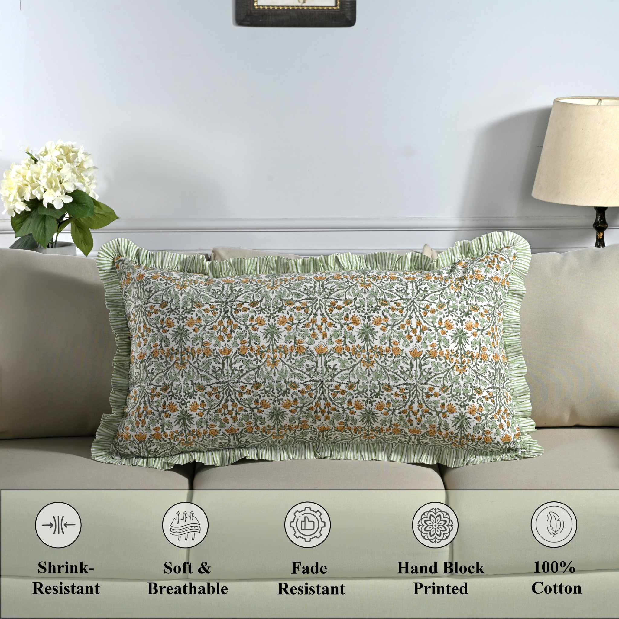 Cotton block print pillow cover placed on a bed with lamp and flowers in background.