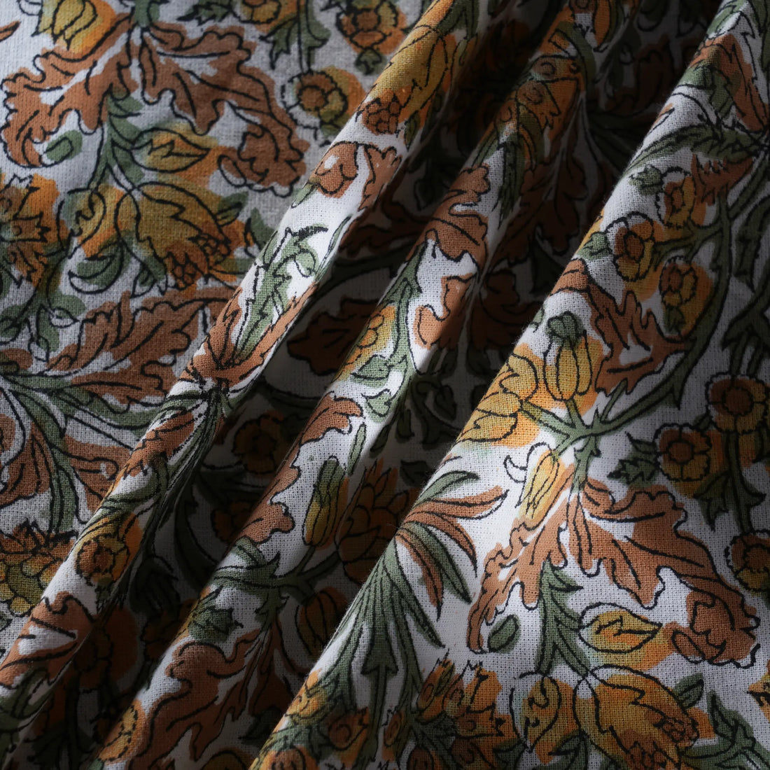 Close-up of floral fabric with orange, green, and brown colors on a white background.