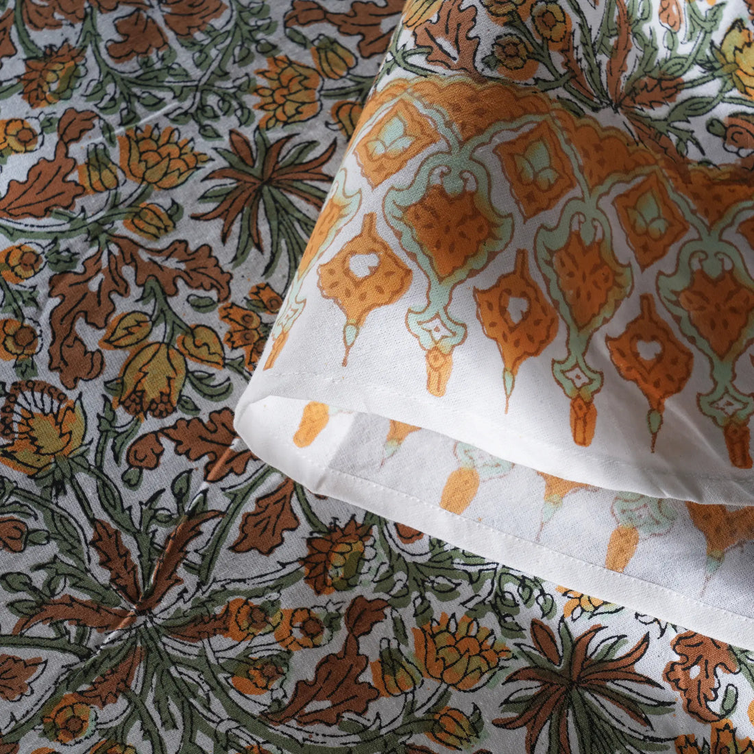Close-up of patterned fabric with orange and green designs on a white background