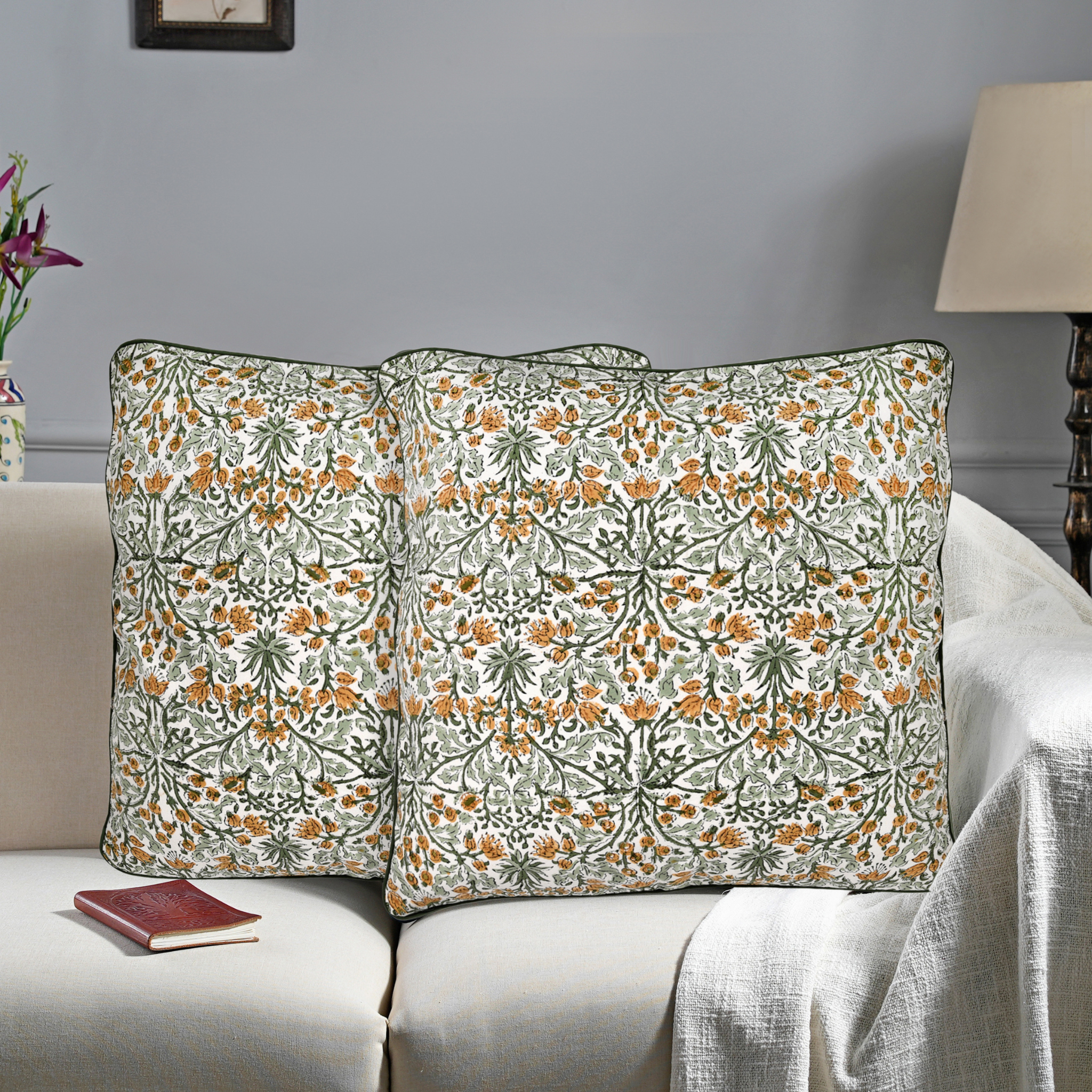 Floral patterned pillows on a sofa with a lamp and flowers in the background.