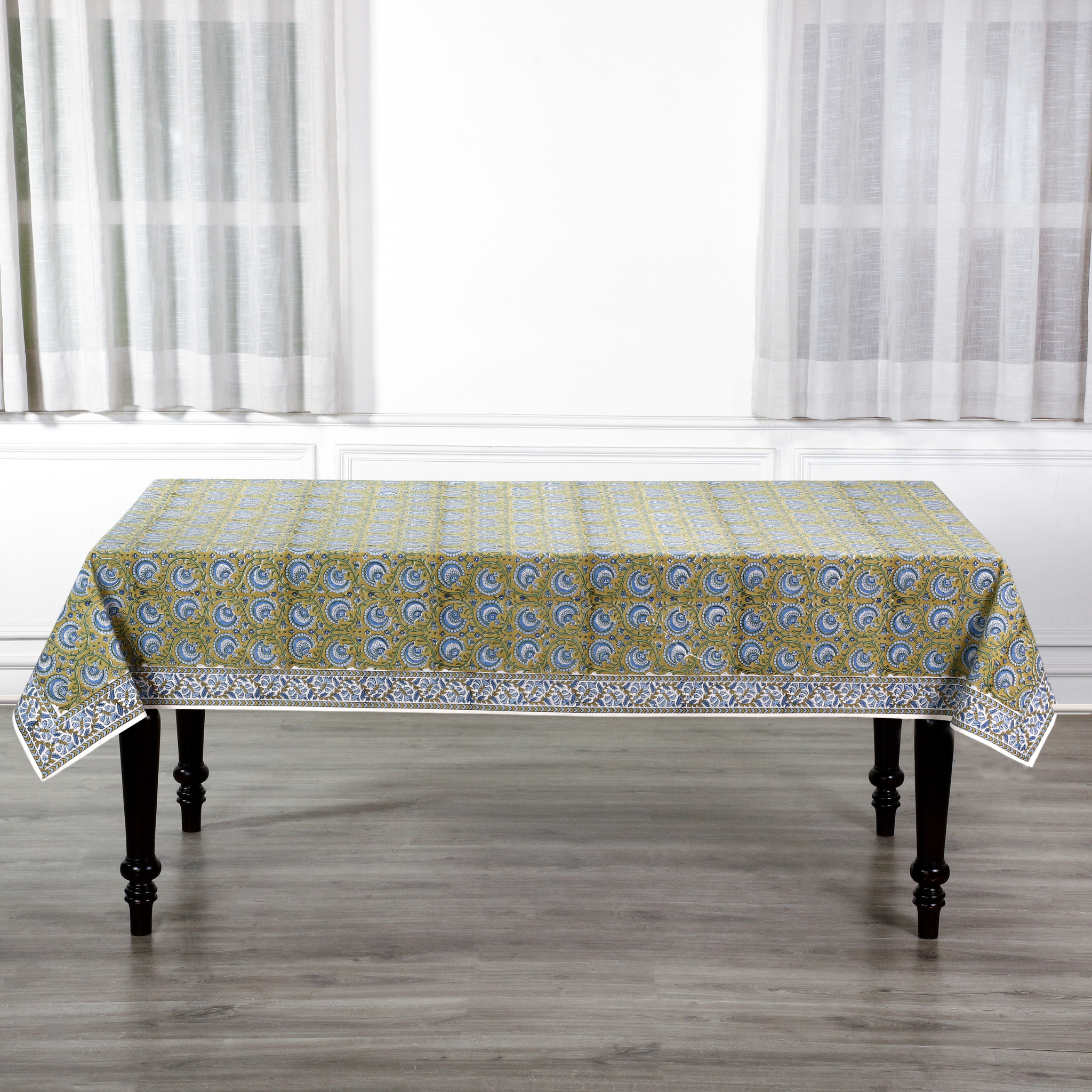 Patterned tablecloth on a wooden table with white curtains in the background