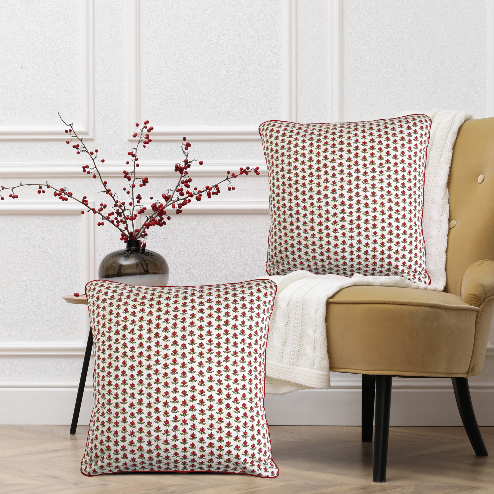 Two patterned pillows on a beige armchair with a vase of red berries on a side table.