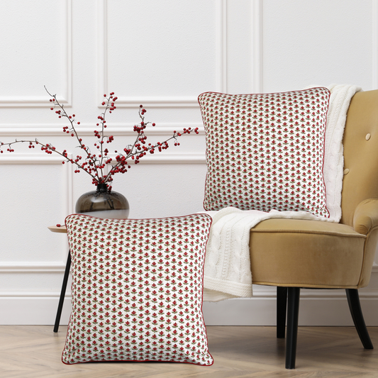 Two patterned pillows on a beige armchair with a vase of red berries on a side table.